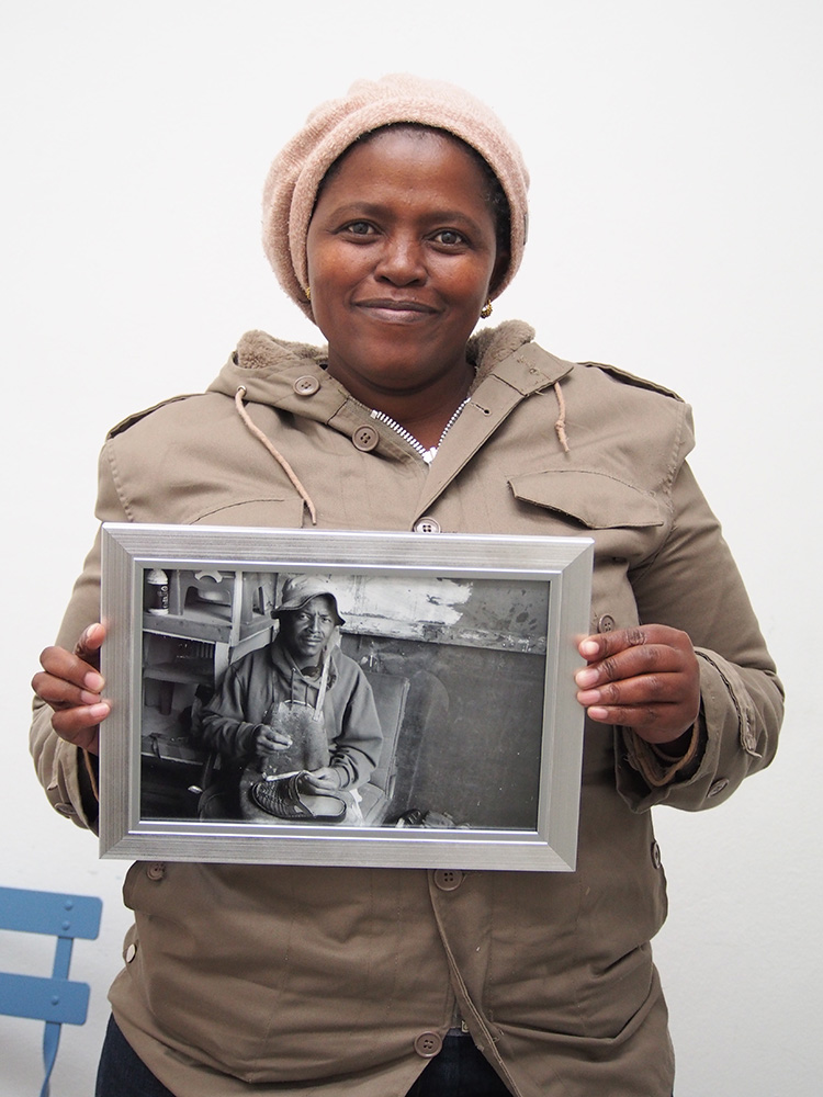 Velisa Wowo, a founding member of The Heart of a Woman Project mobile photography program at eKhaya eKasi proudly displays a framed image of her photo of a shoe repairman in Khayelitsha. This image is Veliswa’s series 1.0 postcard and greeting card and was taken with a donated previously owned iPhone 4s. I surprised the women with framed photos of their ‘postcard images’ in June 2014. They are on display at eKhaya eKasi and were admired by the community and guests at the 1st anniversary photography exhibition and cultural celebration at the centre on November 22, 2014.