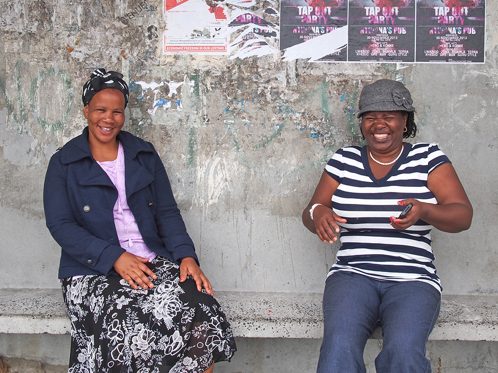 Participants, Yolanda Nkatula and Esther Mahlasela share a laugh at a bus stop in Khayelitsha.